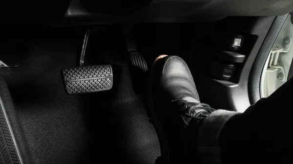 Conductor presionando el pedal del freno en un coche, activando el sistema de frenos.
