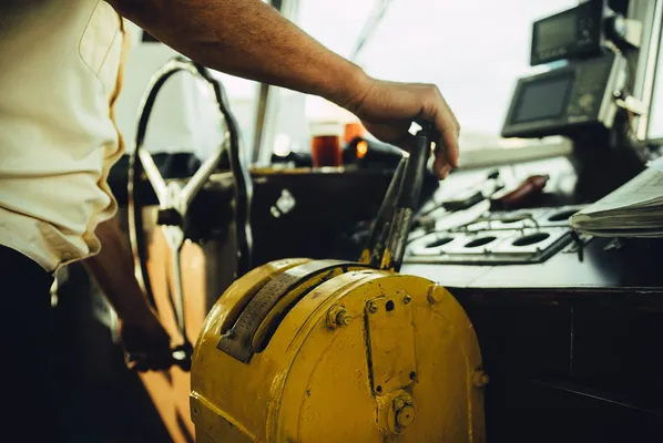 Fotografía de una palanca de motor para barco en color amarillo con el comandante visible en segundo plano durante la navegación