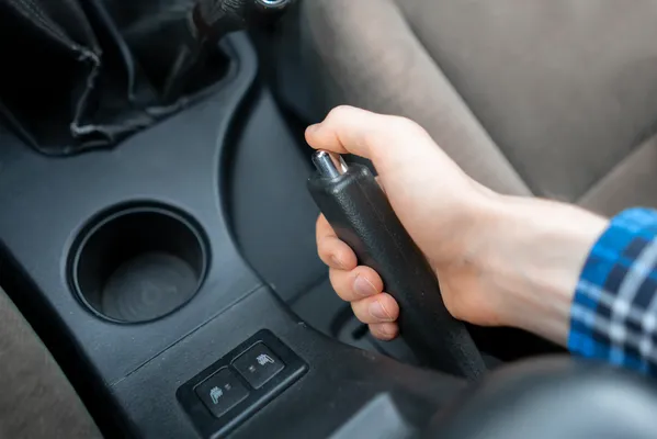 Mano de conductor levantando el freno de mano en un sistema automotriz que utiliza cables mecánicos de tracción