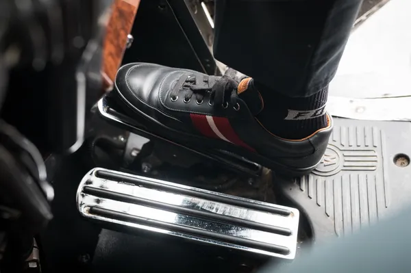 Persona pisando el pedal del clutch en un automóvil con sistema mecánico activado por cables automotrices