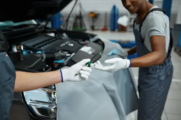 Dos mecánicos colaborando en la reparación de un auto mientras intercambian herramientas para realizar el procedimiento de cómo cambiar chicote de clutch